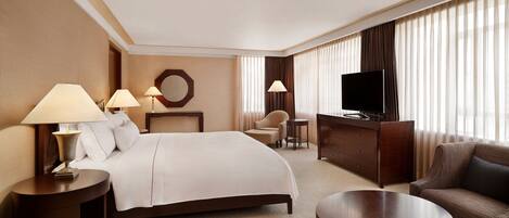 A hotel room with a large bed, two bedside tables with lamps, a TV, a sofa, and a small round table.
