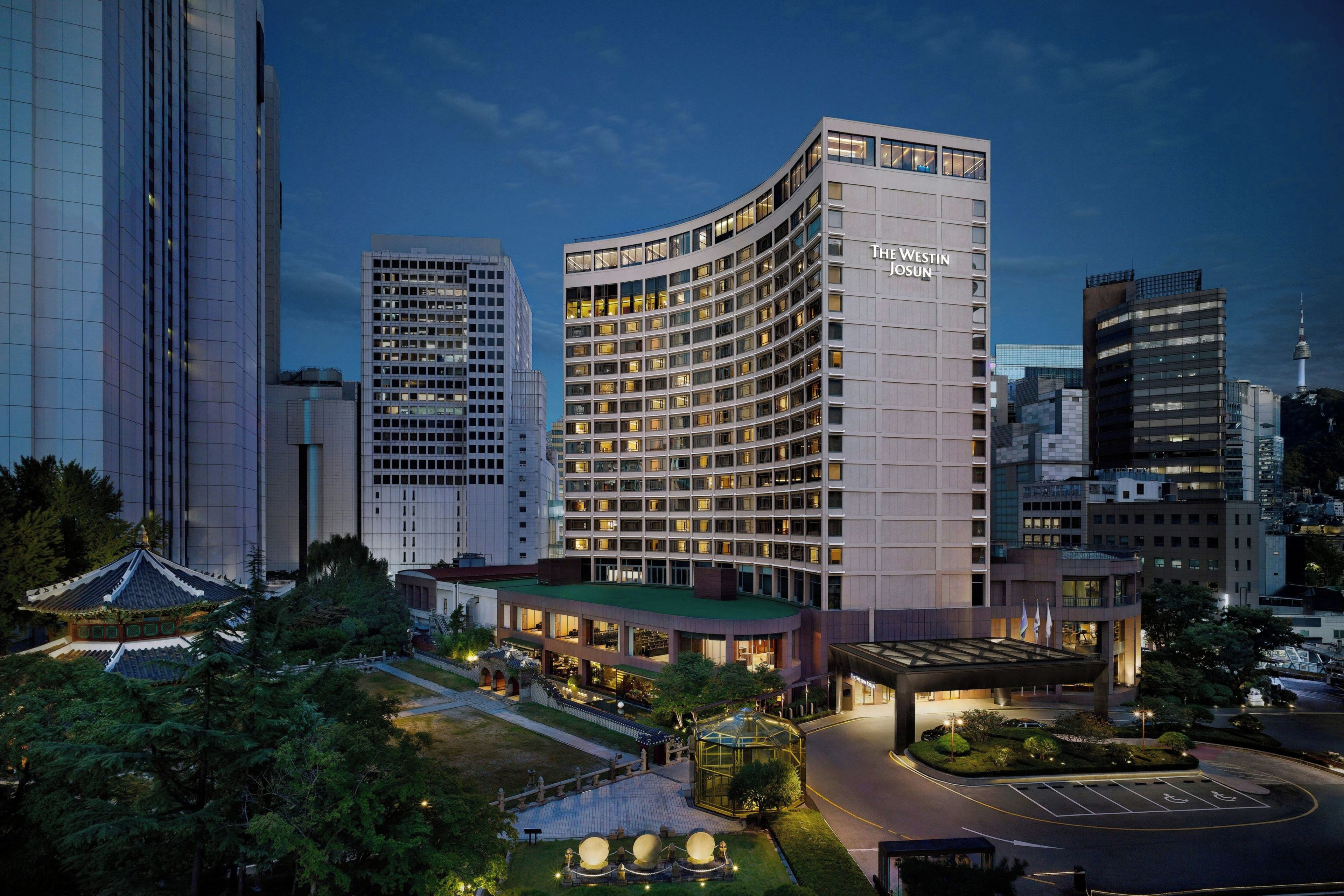 A modern hotel with a curved facade, multiple floors, and a well-lit entrance area.
