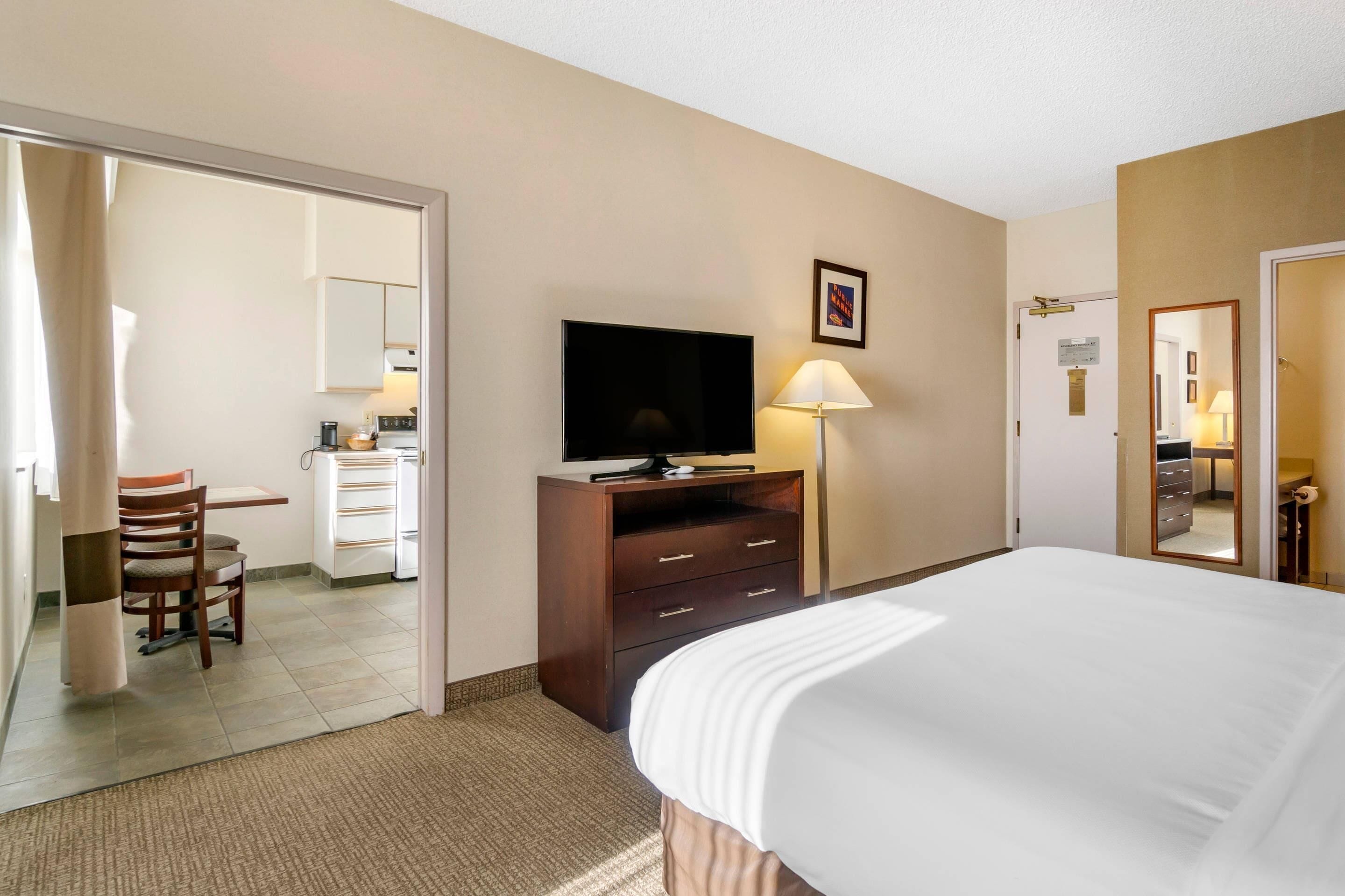 A hotel room with a bed, a television, a desk with a chair, a lamp, and a wardrobe.