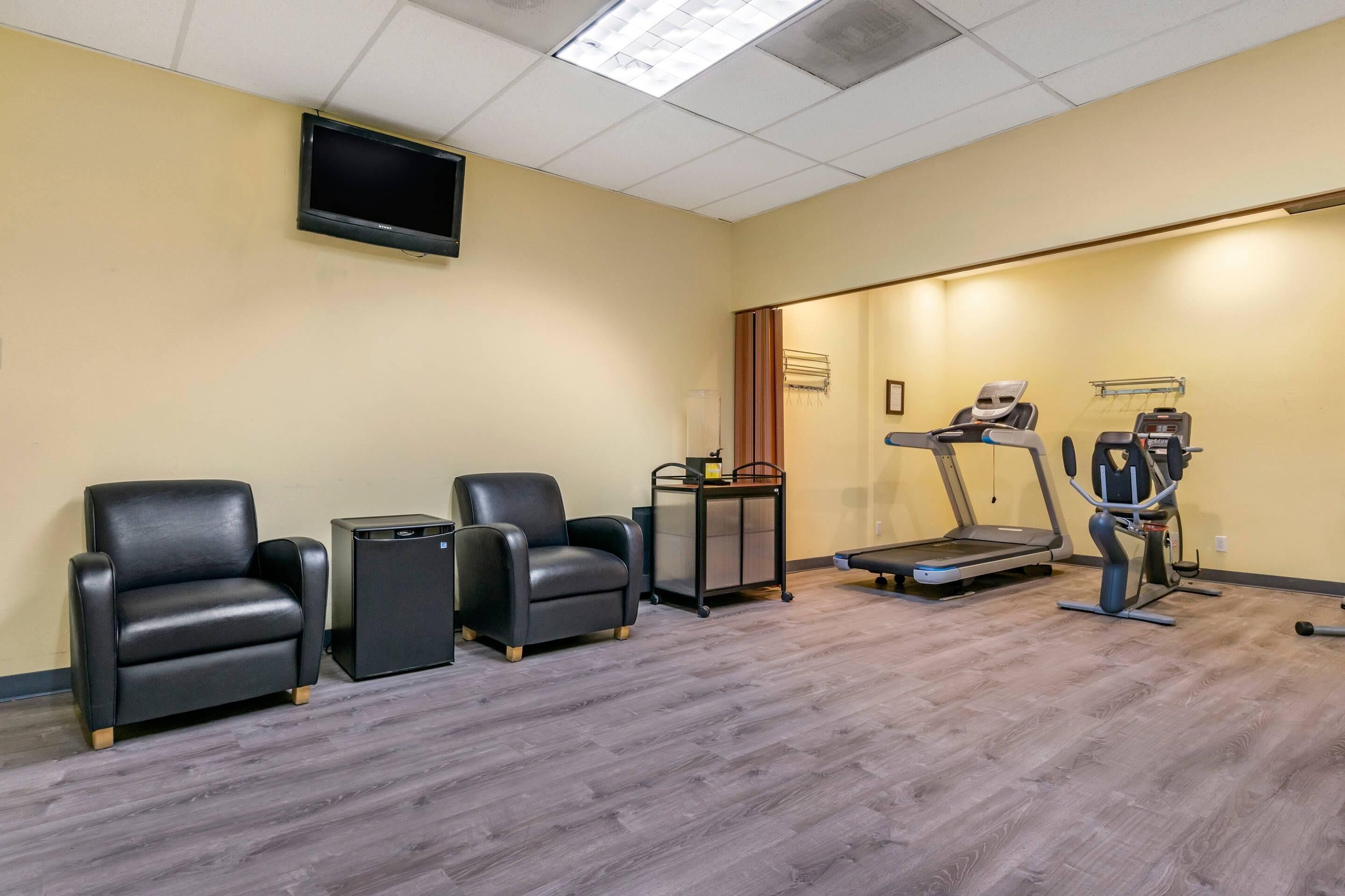 A room with a treadmill, two massage chairs, a small table, and a television mounted on the wall.