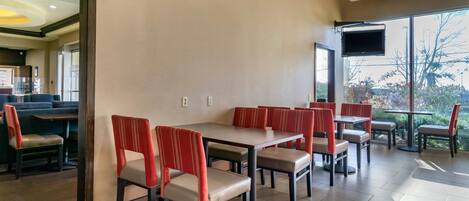 Un restaurante con cabinas y mesas, un televisor de pantalla plana y vistas a árboles y al cielo.
