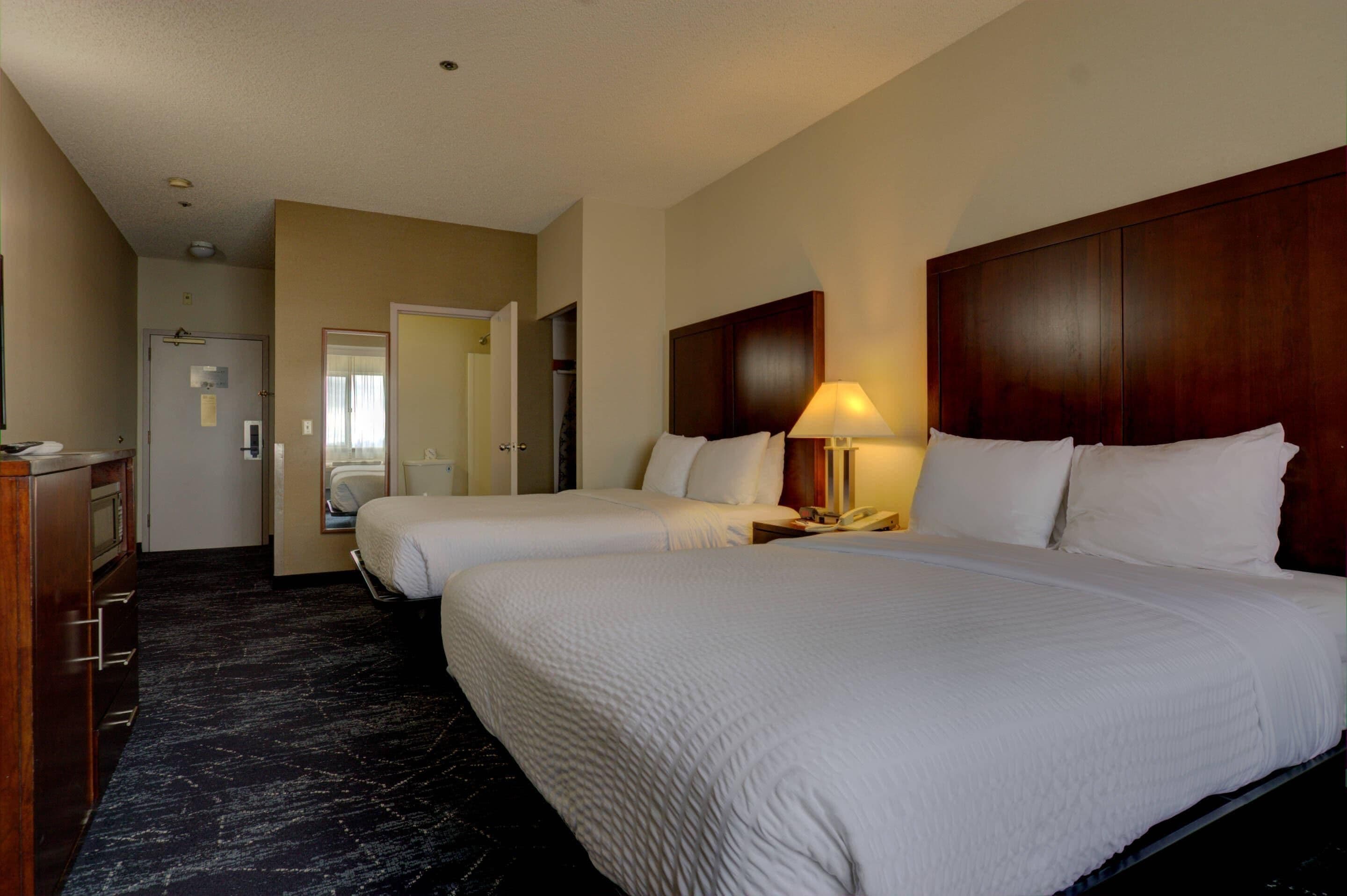 A hotel room with two beds, a wooden headboard, a bedside lamp, a desk, and a wardrobe.