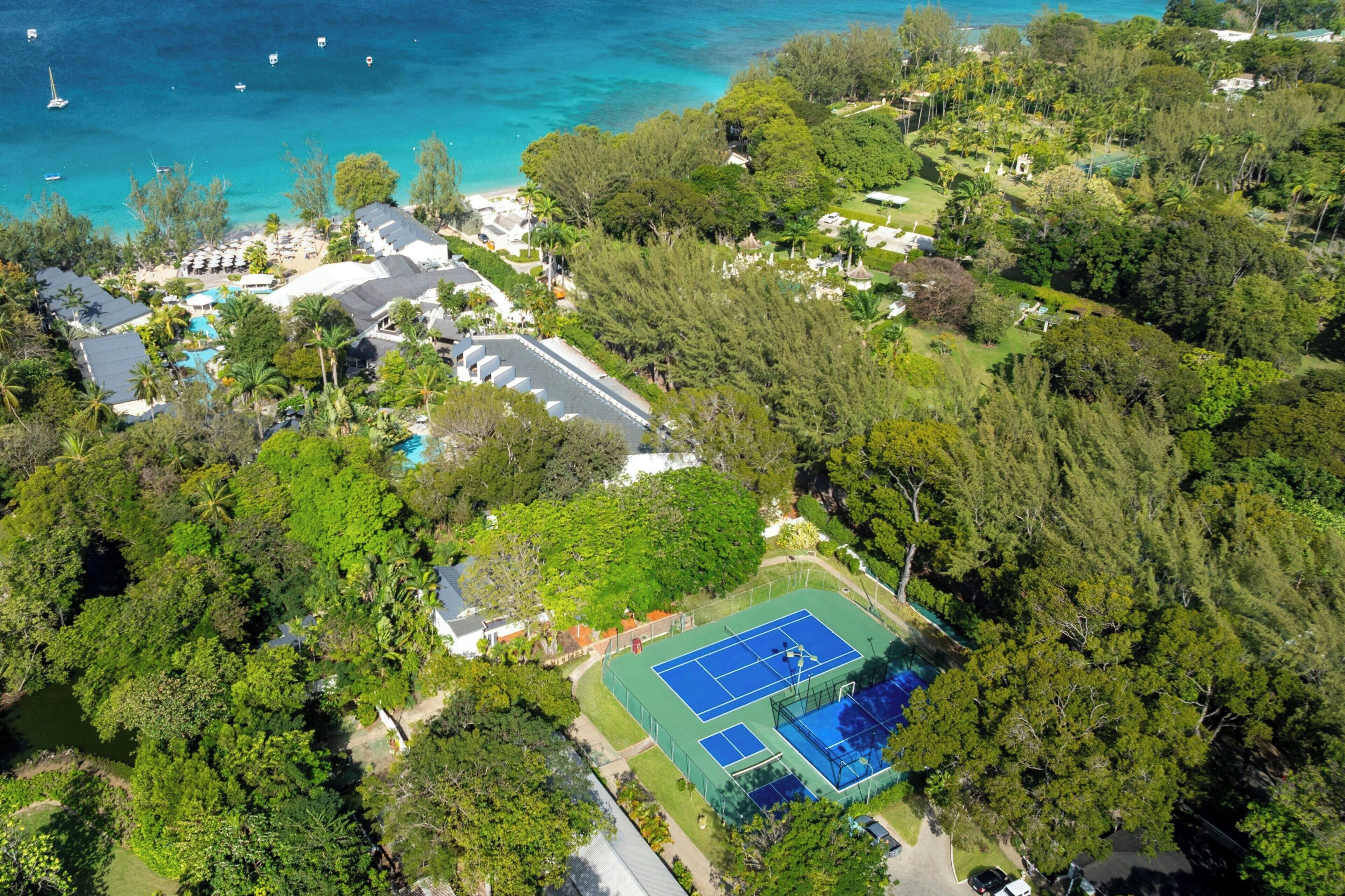 Eine Luftaufnahme eines Resorts mit Tennisplatz, Pool und direktem Strandzugang.