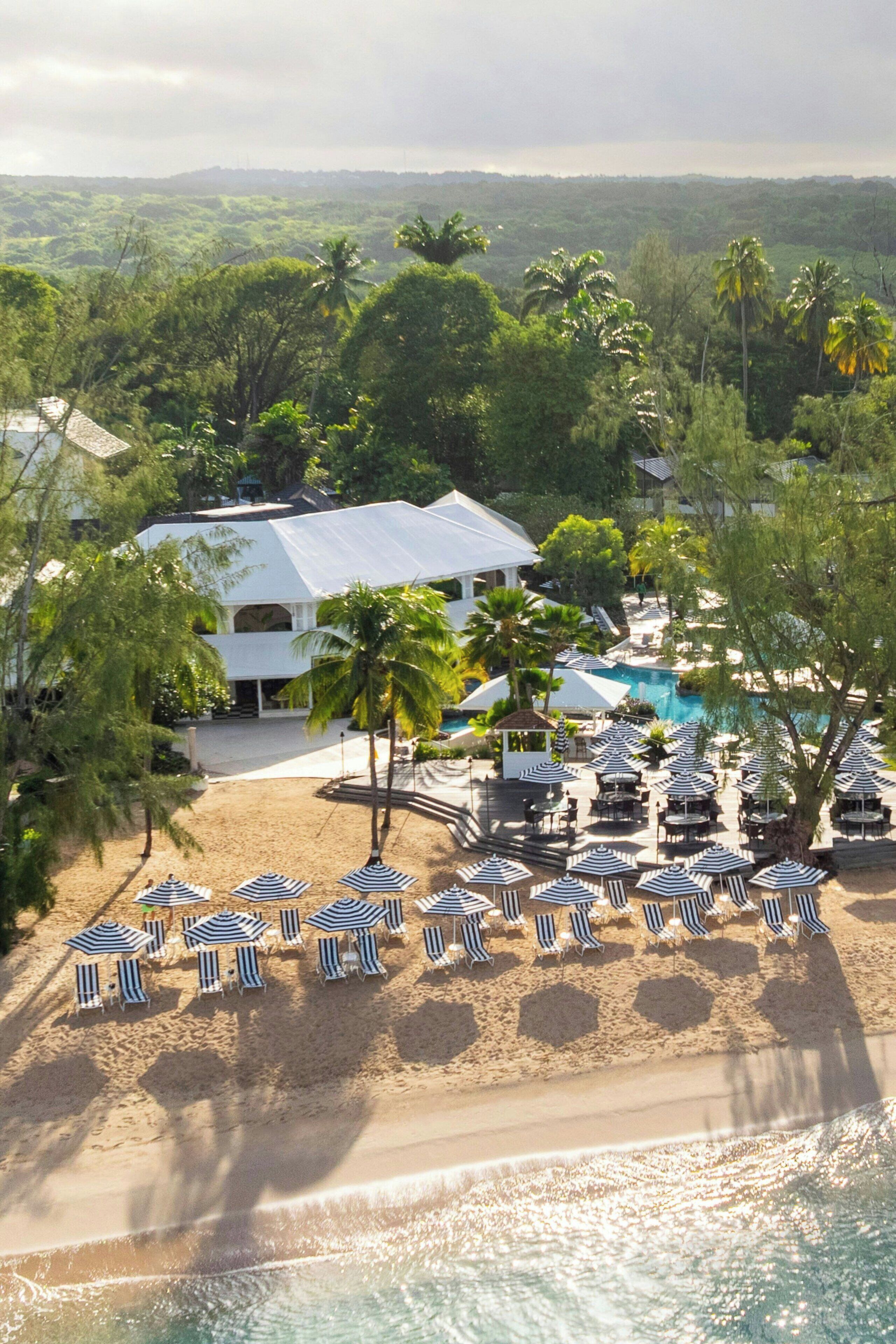 A resort with a pool, beach chairs, umbrellas, and palm trees.