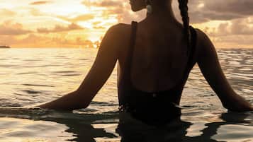 A person standing in water with a sunset in the background.