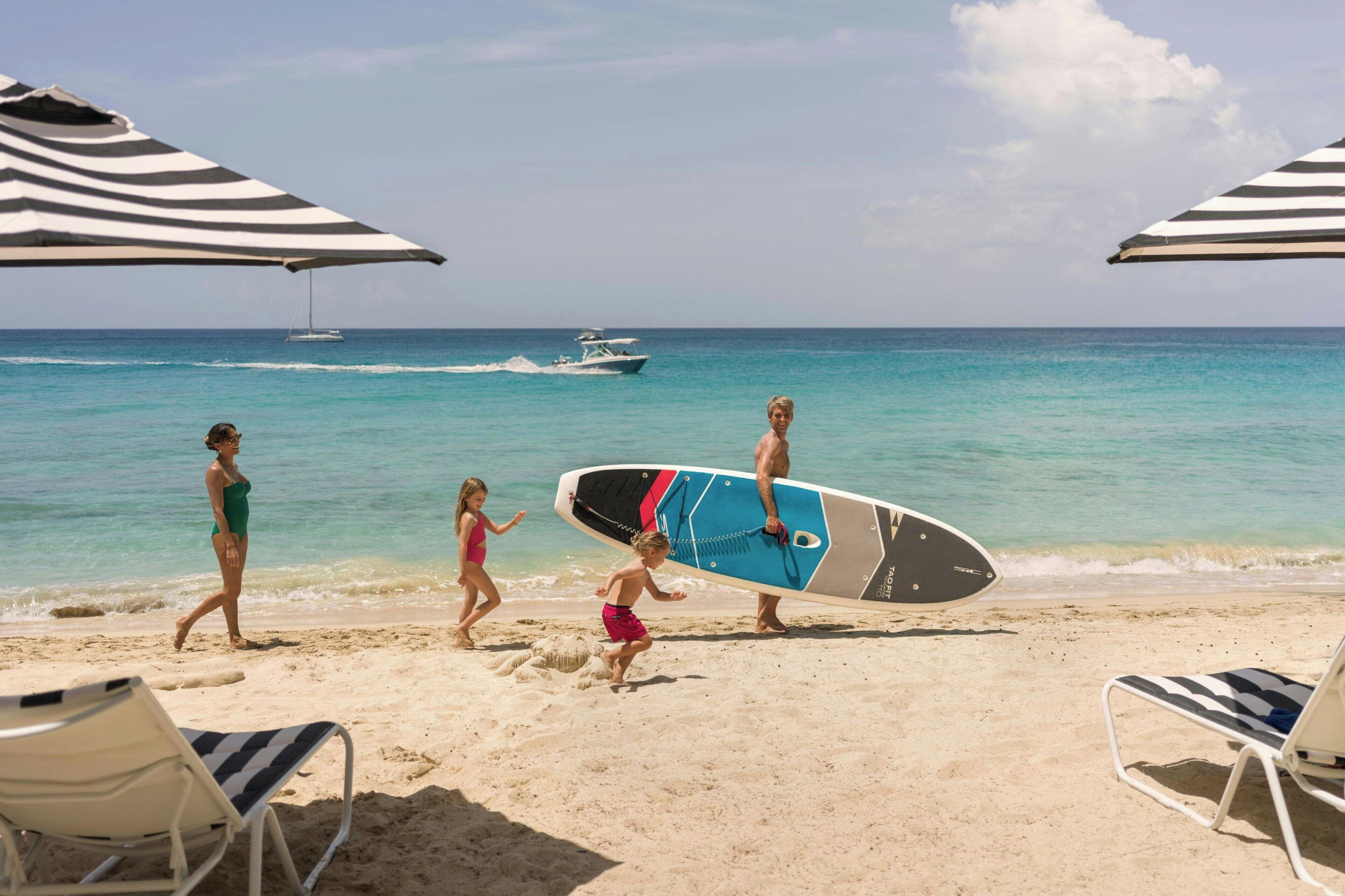 A beach with a surfboard, a sailboat, and beach chairs.