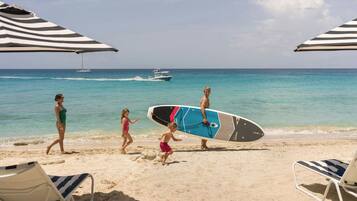 A beach with a surfboard, a sailboat, and beach chairs.