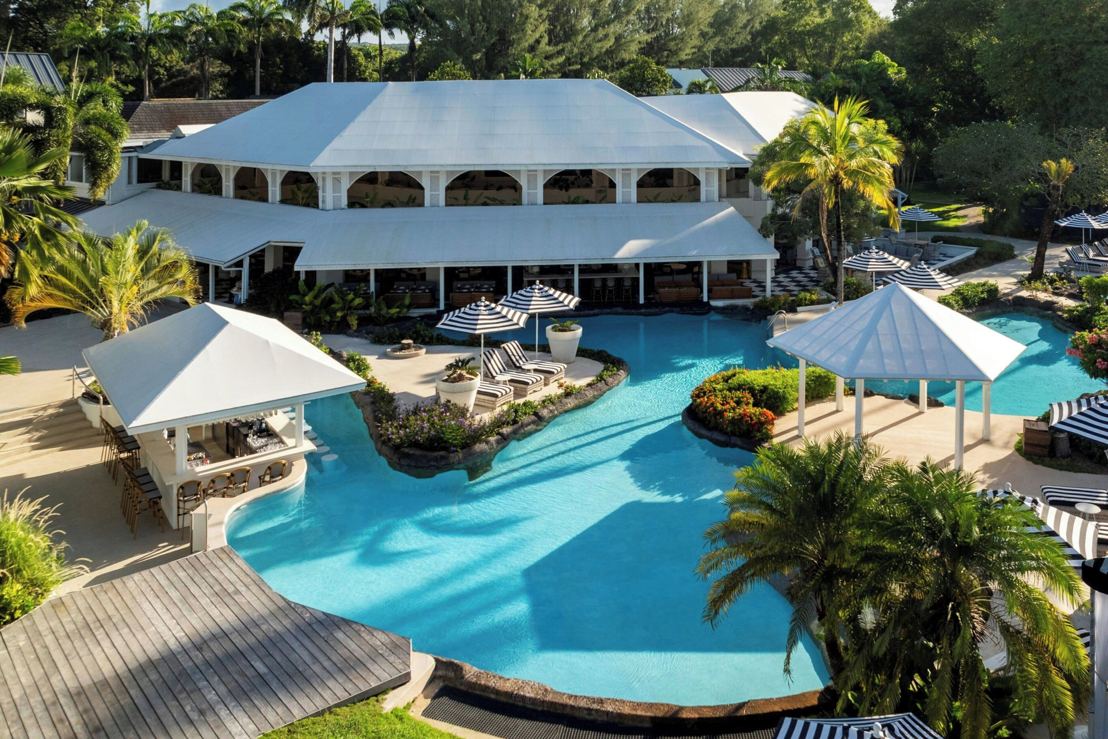 Un resort con una gran piscina, áreas de descanso con sombrillas y una zona de estar cubierta.