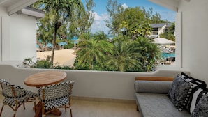 Un balcon donnant sur une plage, une table ronde en bois, deux chaises à motifs et un canapé avec des coussins à motifs.
