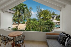 Un balcón con vista a la playa, una mesa redonda de madera, dos sillas estampadas y un sofá con cojines decorativos.
