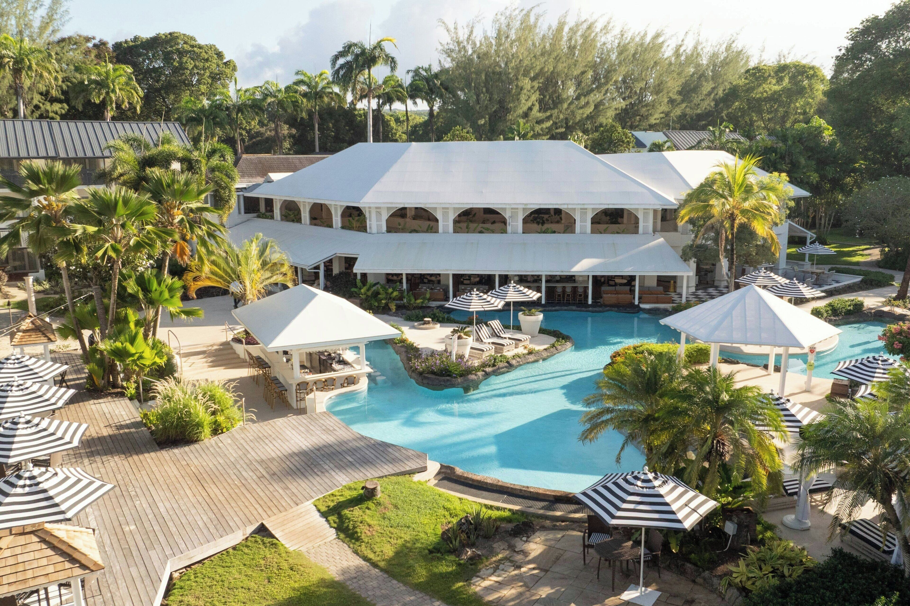 Un resort con una amplia piscina, áreas de descanso con sombrillas y un edificio central de techo blanco.