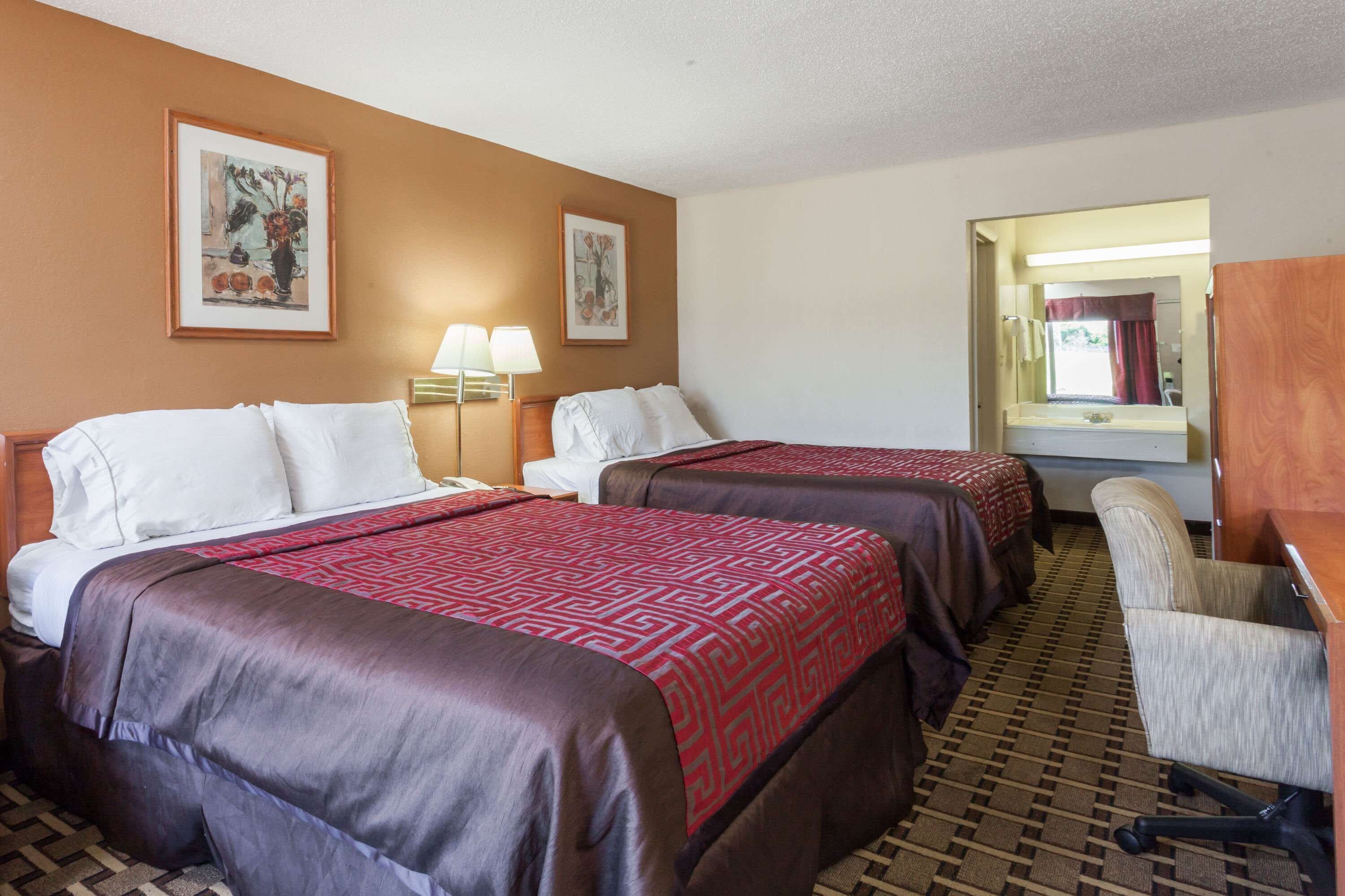 A hotel room with two beds, a desk, a chair, and two wall-mounted lamps.