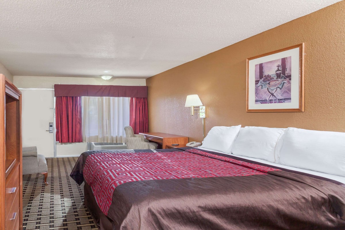 A hotel room with a large bed, a desk, a chair, and a painting on the wall.