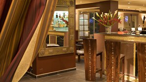 A bar area with a mirror, bar stools, and a vase of flowers. - Beausejour (Cannes)