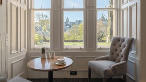 A room with a large window, a round table with a cup and saucer, and a tufted armchair. - Old Waverley Hotel (Edinburgh)