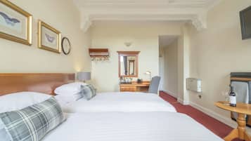 Hotelkamer met twee bedden, een bureau, een stoel, een spiegel en een tafeltje met een fles en een glas.