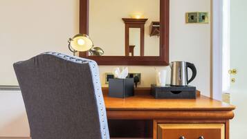 Ein Hotelzimmer mit Schreibtisch aus Holz, einem Sessel, einem Spiegel, einer Kaffeemaschine und einer Taschentuchbox.