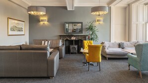 A living room with a fireplace, sofas, a yellow chair, and wall-mounted lamps. - Old Waverley Hotel (Edinburgh)