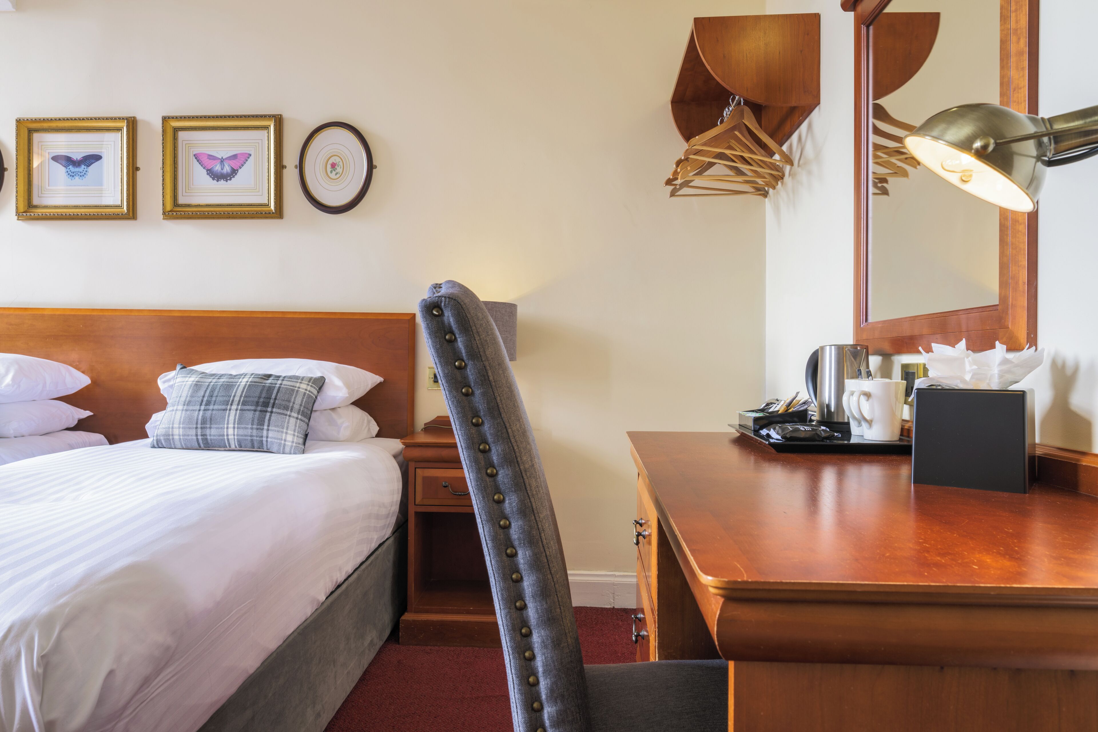 Habitación de hotel con cama, escritorio, silla, lámpara, espejo y cuadros en la pared.