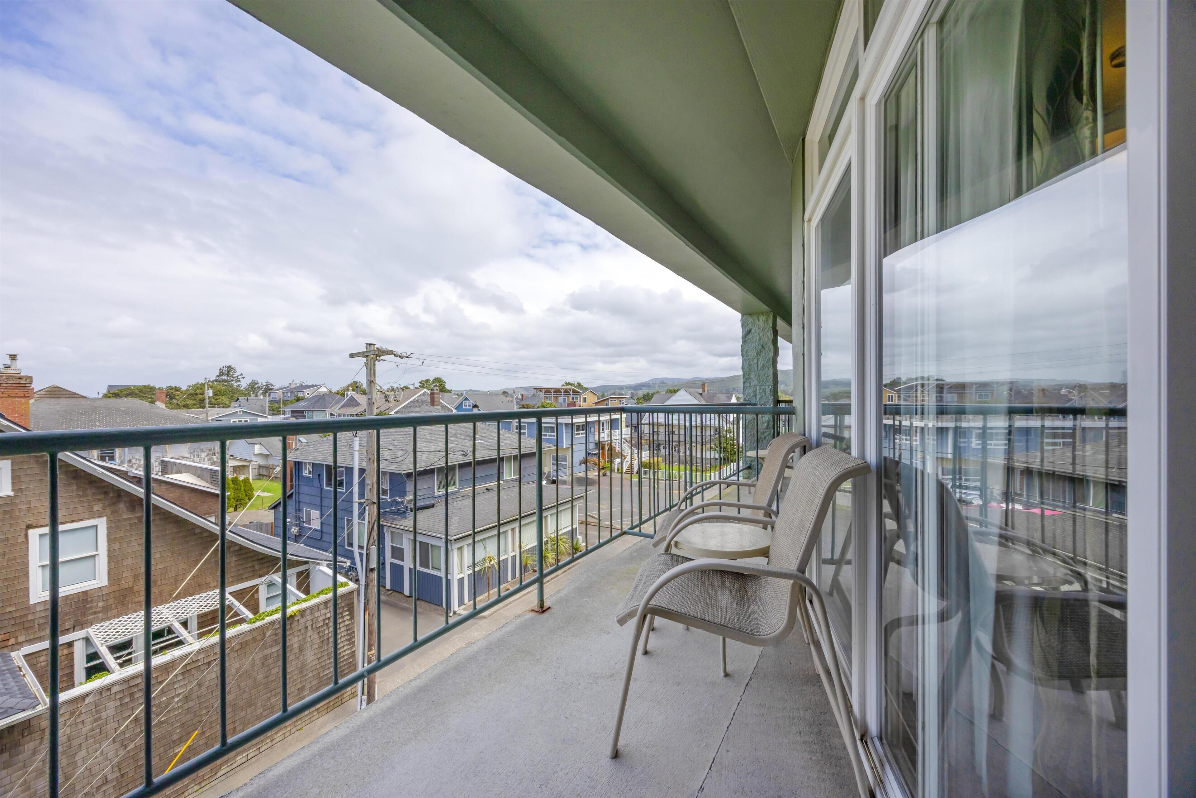 A balcony with a view of residential buildings, a metal railing, and two chairs.