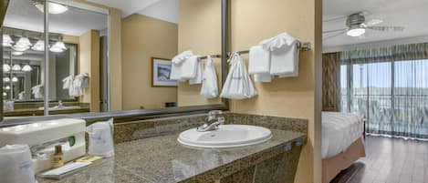 Ein Hotelbad mit einem Waschbecken mit Granittheke, einem großen Spiegel und einem Deckenventilator.