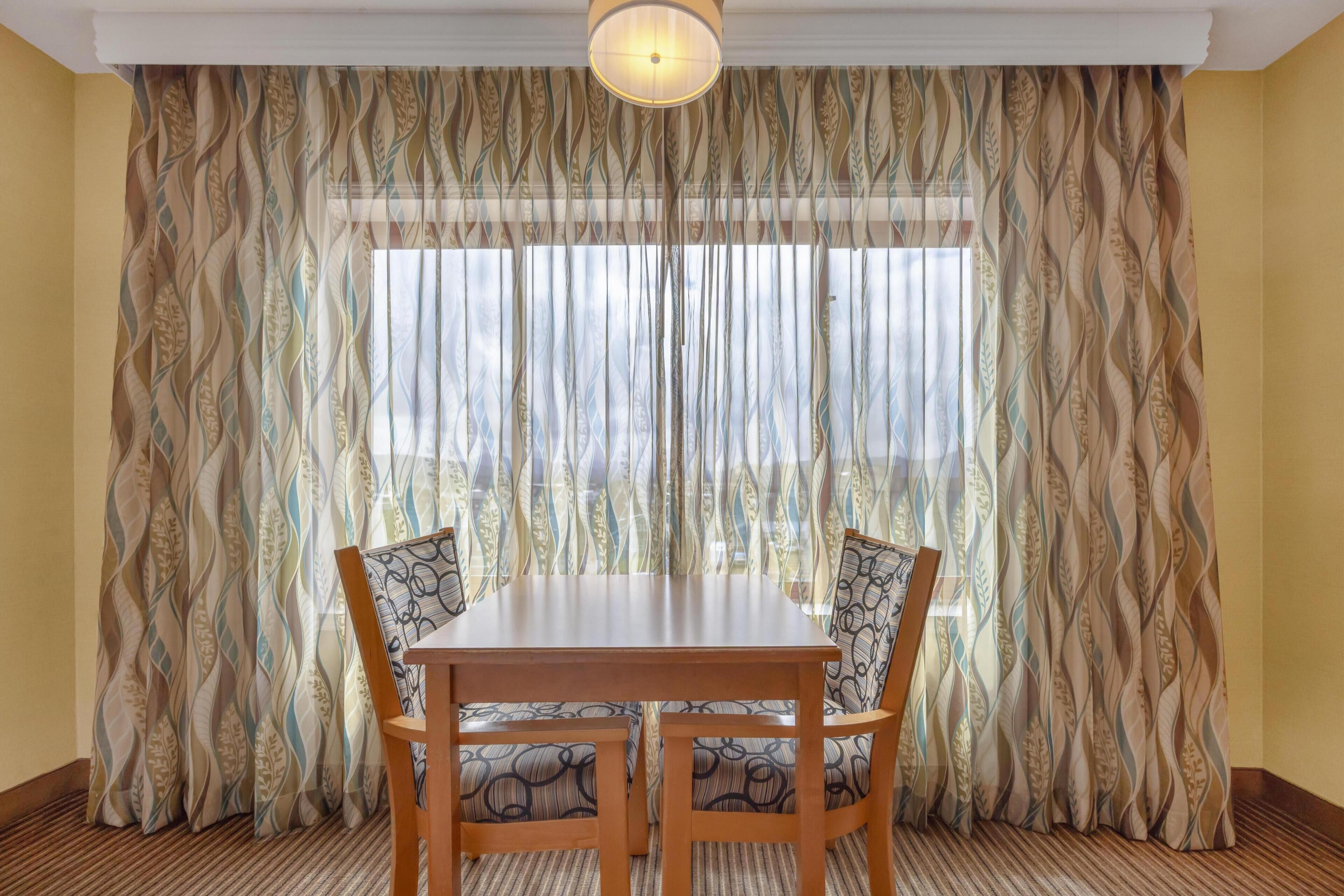 Un comedor con mesa y sillas, un cortinero estampado y una ventana con persianas.