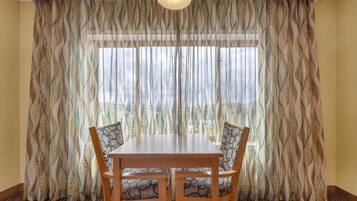 A dining area with a table and chairs, a patterned curtain, and a window with blinds.