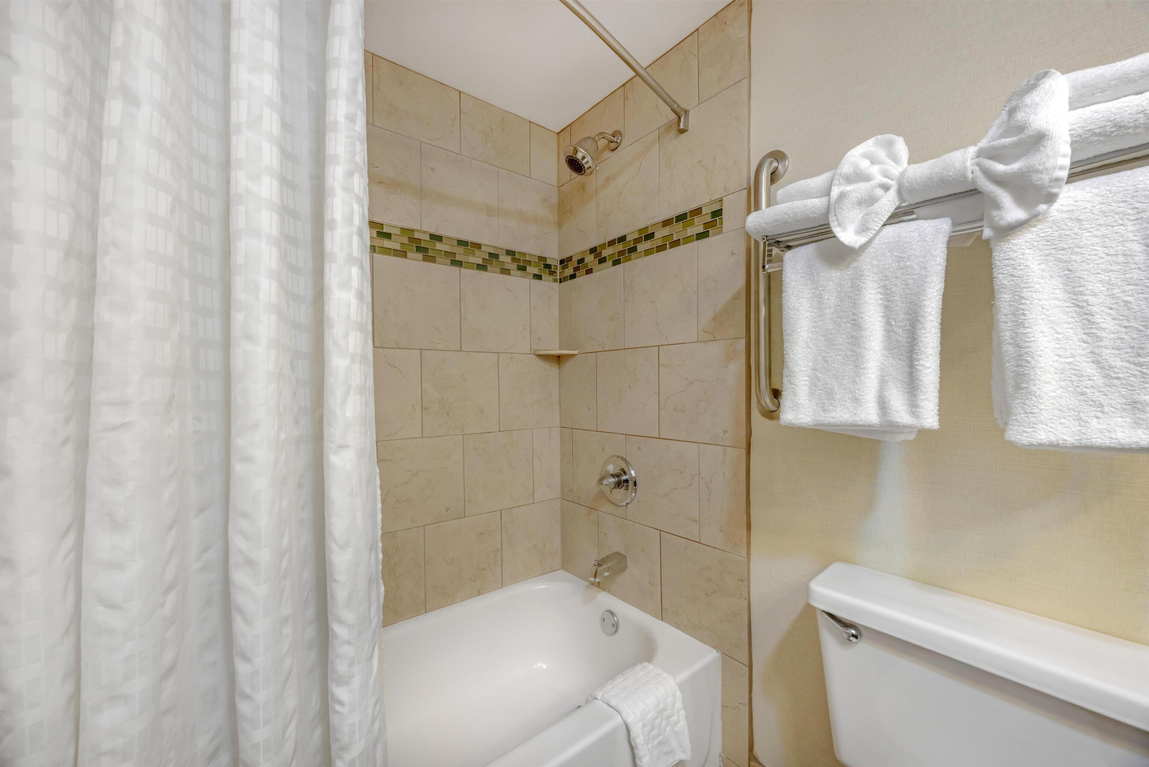 A bathroom with a bathtub, shower, toilet, and towel rack with towels.