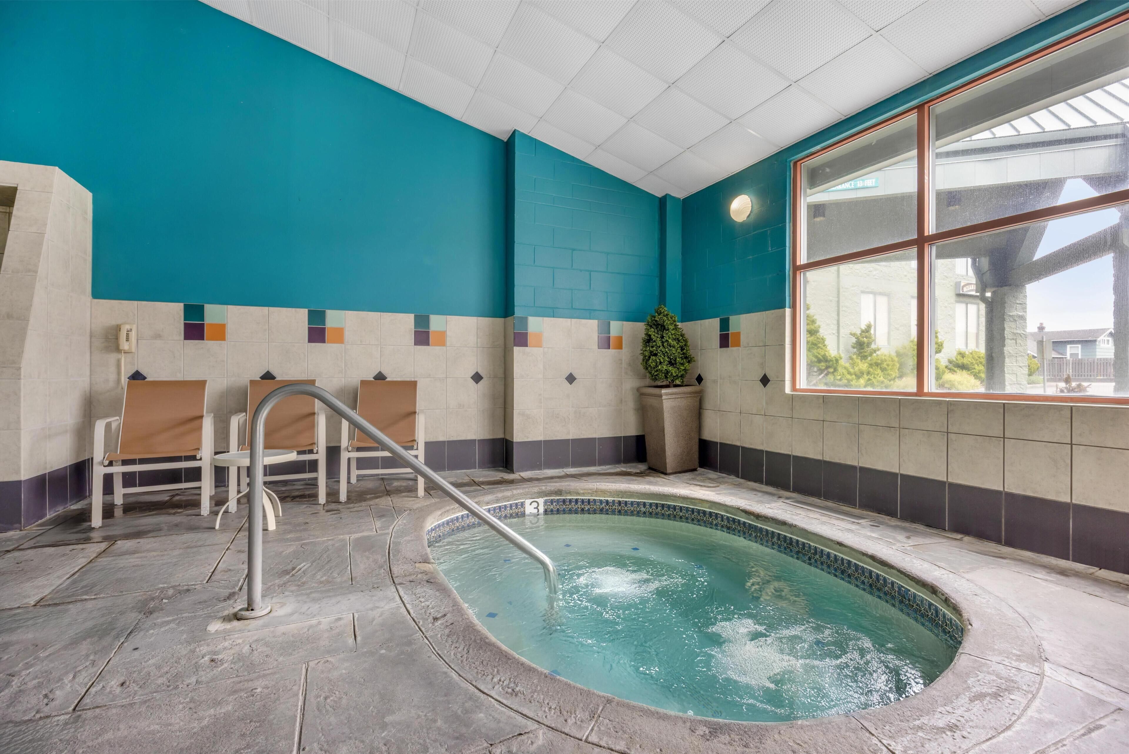 Una piscina interior con suelo de baldosas, barandilla metálica y ventana con vistas al exterior.