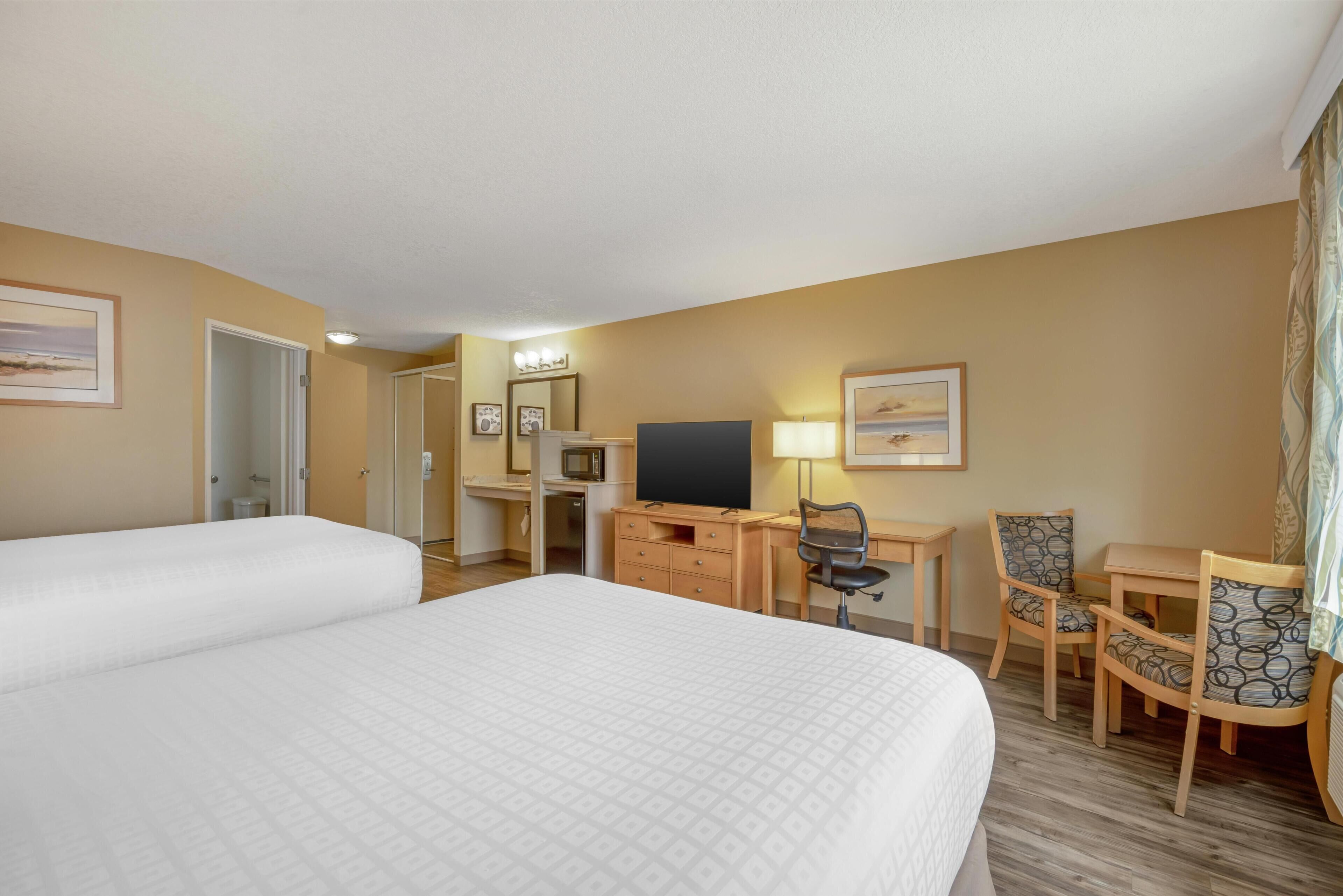 Une chambre d’hôtel avec deux lits, un bureau avec une chaise, une télévision et une lampe.
