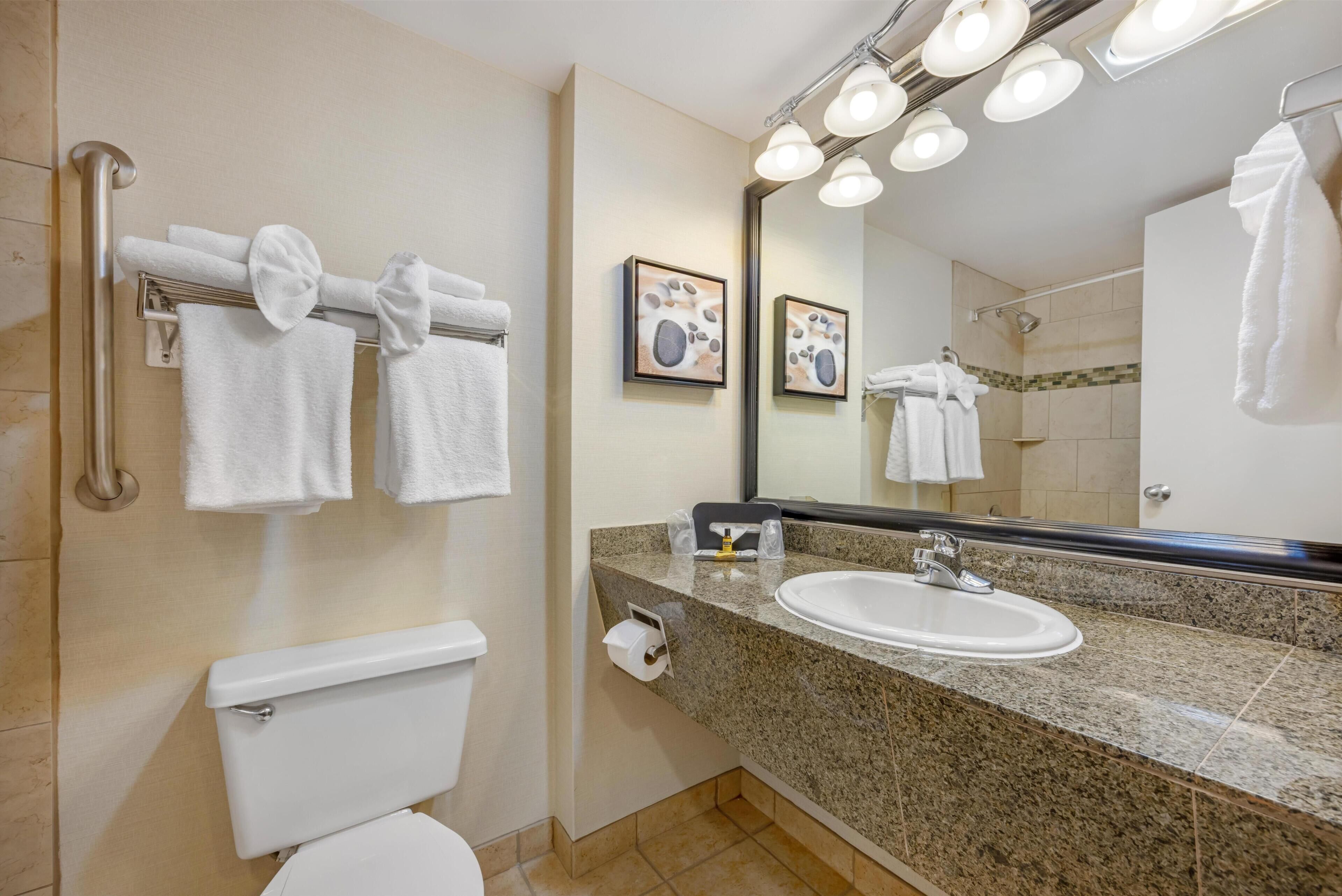A bathroom with a toilet, sink, towel rack, and a large mirror with lights.