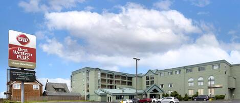 A hotel with a large sign advertising 'Best Western Plus Ocean View Resort,' a parking lot with several cars, and a building with a green facade.