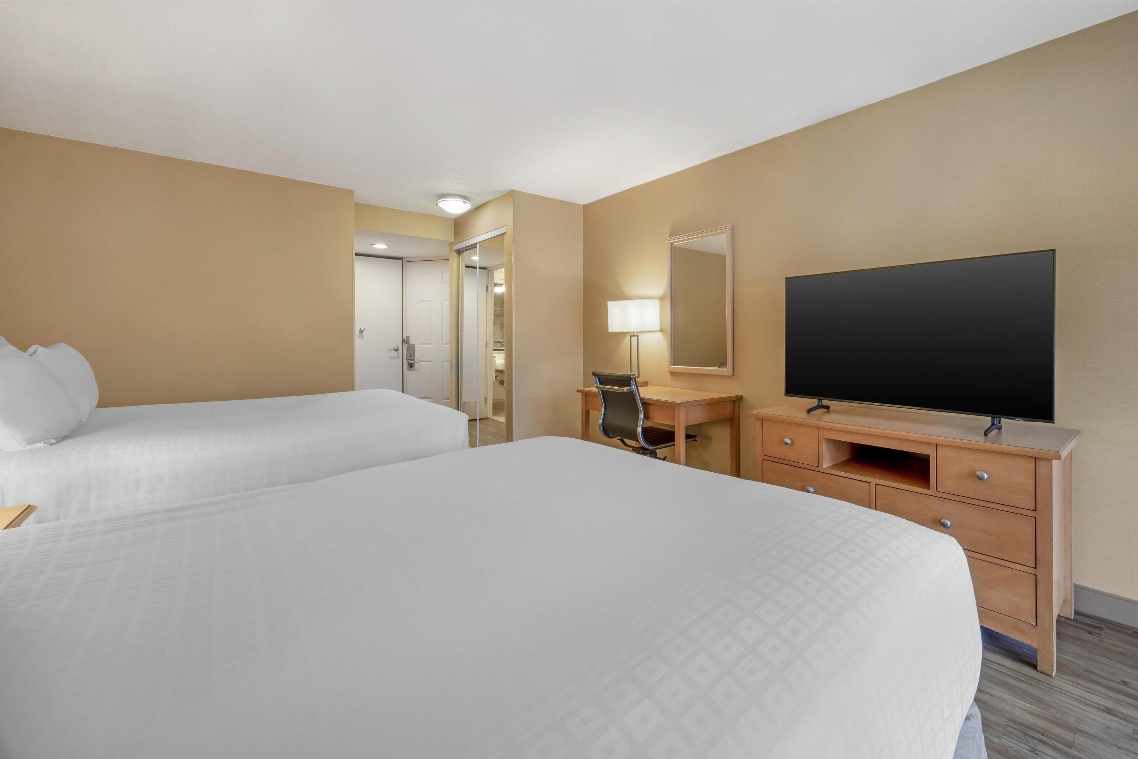 Ett hotellrum med två sängar, ett skrivbord med en lampa, en TV och en spegel.