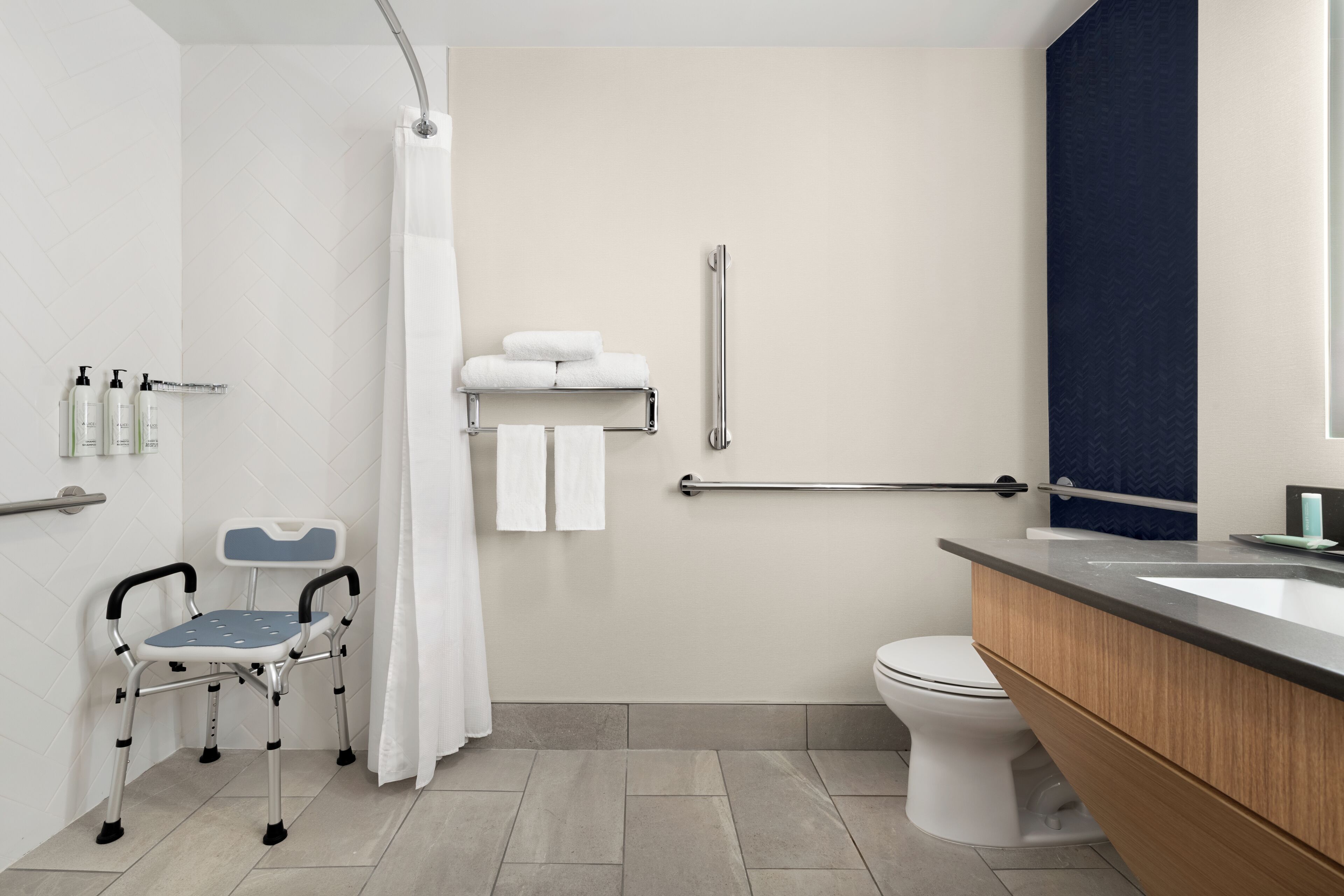 Un baño moderno con ducha, inodoro y una barra de apoyo cerca del lavabo.