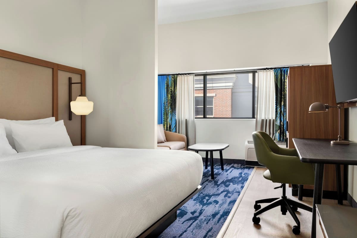 Ein Hotelzimmer mit einem großen Bett, einem Schreibtisch mit Stuhl, einem kleinen Tisch und einem Fernseher.