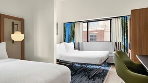 A hotel room with two beds, a desk, and a chair.