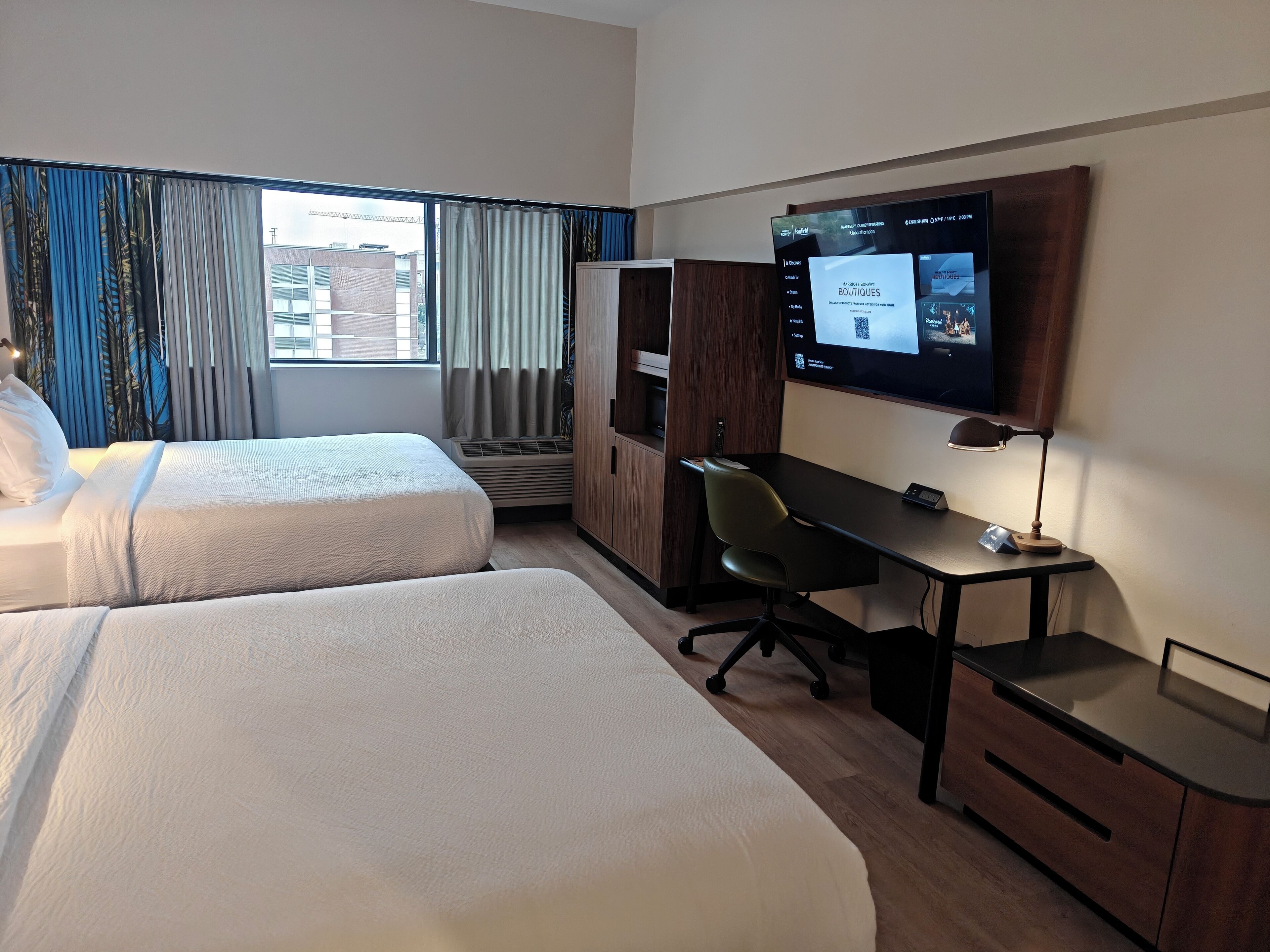 Habitación de hotel con dos camas, un escritorio, una silla, un televisor y un armario.