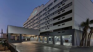 A modern hotel with a flat roof, multiple floors, and a large parking area.
