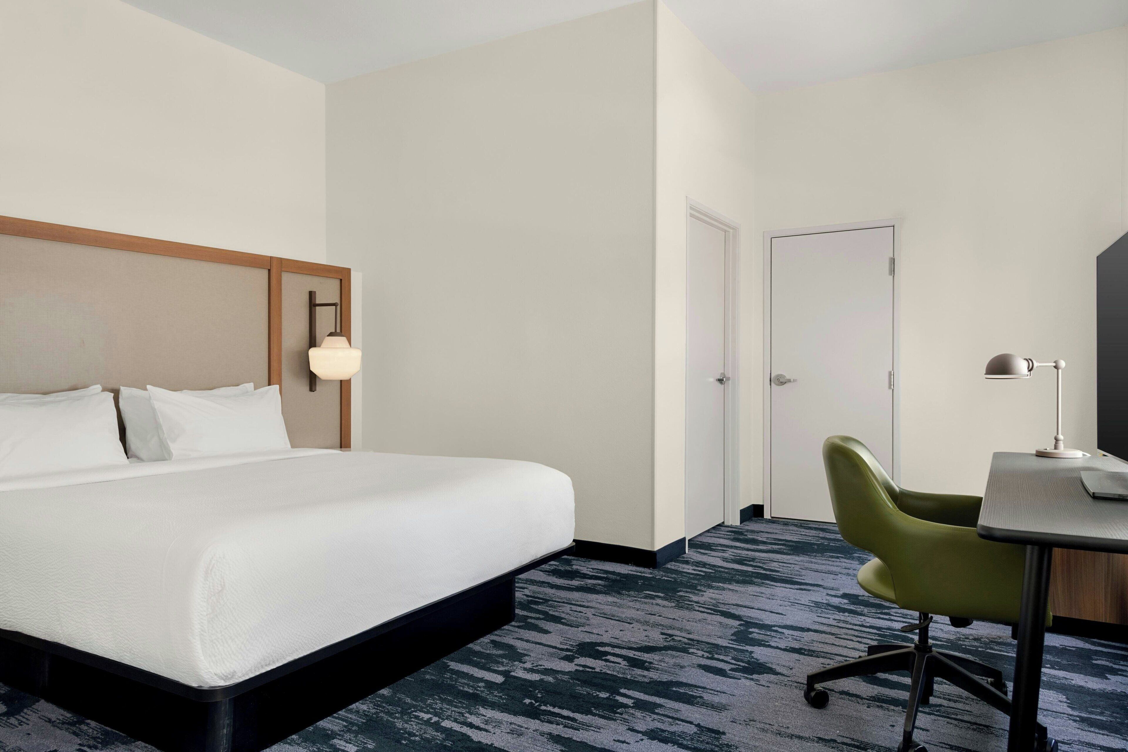 A hotel room with a bed, a desk, a chair, and a door.