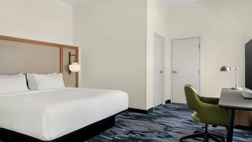 A hotel room with a bed, a desk, a chair, and a door.