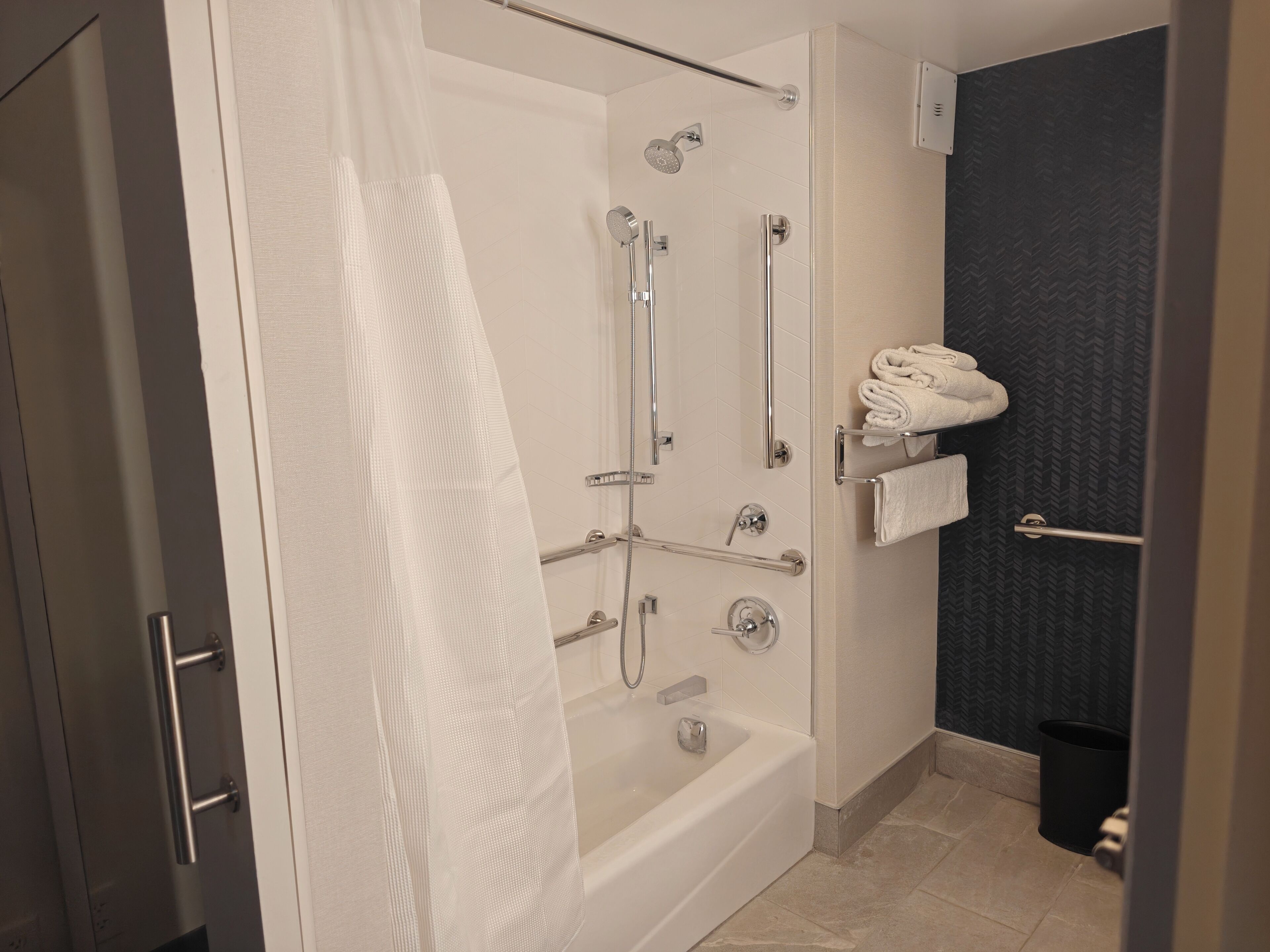 A modern bathroom with a glass shower enclosure, a bathtub, and a towel rack with folded towels.