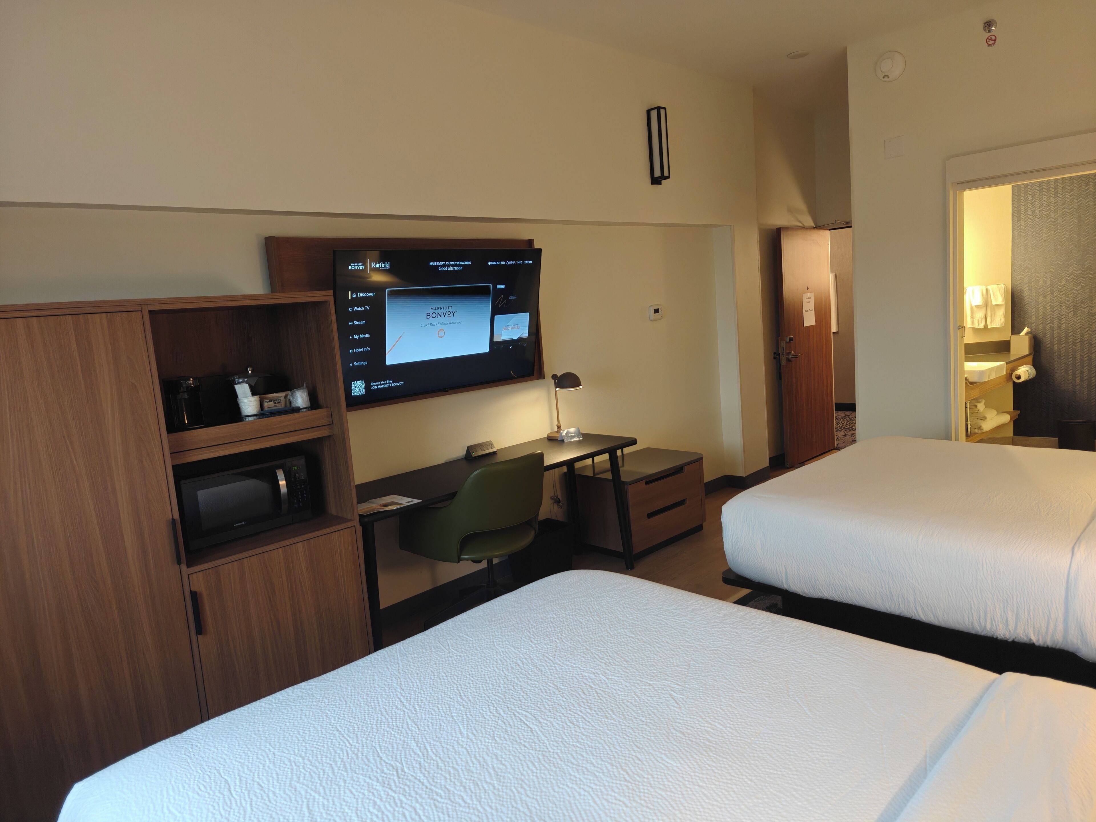 Ein Hotelzimmer mit zwei Betten, einem Schreibtisch mit Computer, einem Fernseher und einer Minibar.