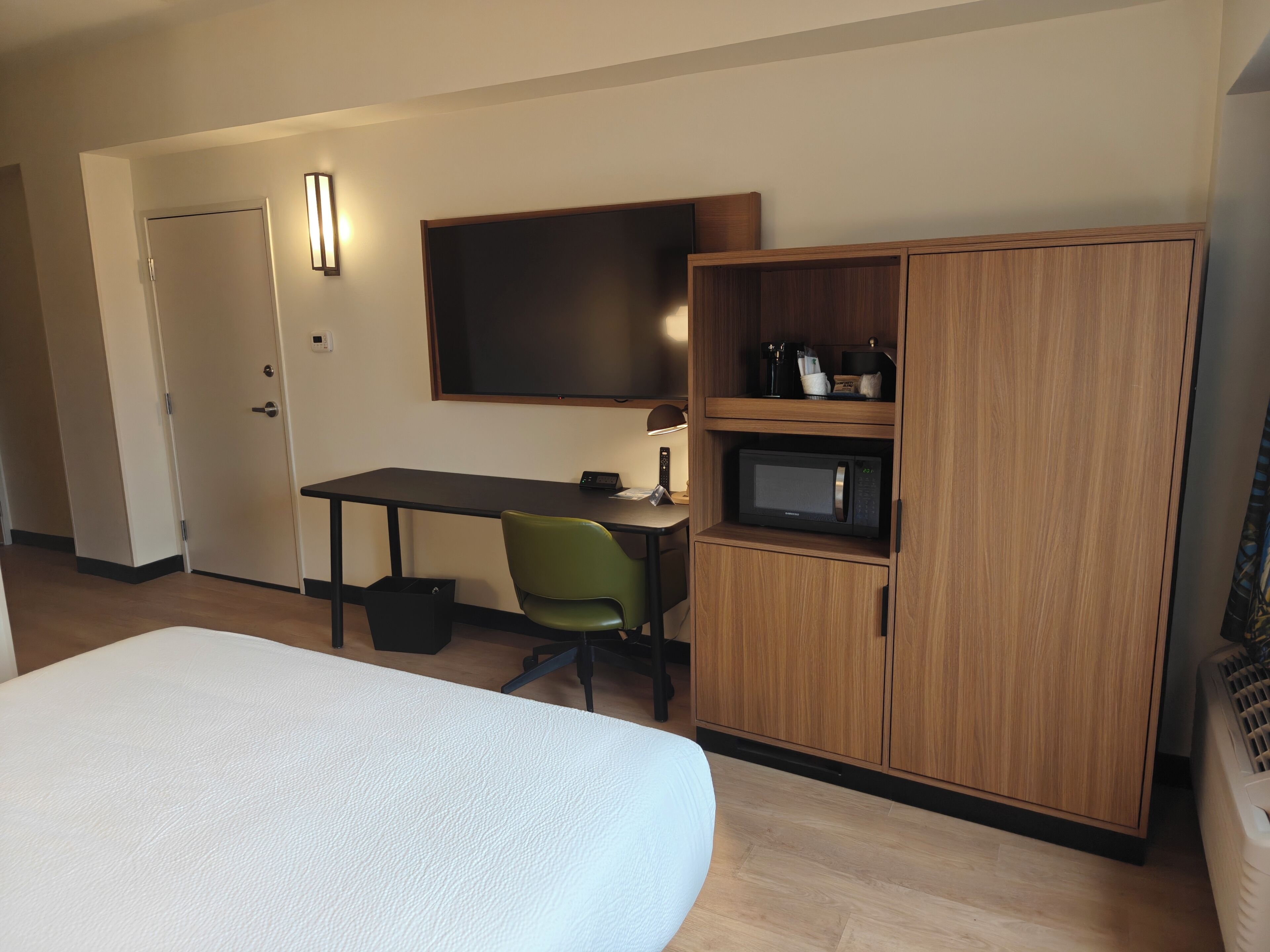 Une chambre d’hôtel avec un lit, un bureau, une chaise verte, un four à micro-ondes et un placard.