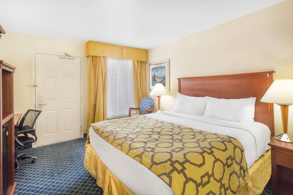 Une chambre d’hôtel avec un lit, un bureau, une chaise, une lampe et une porte.