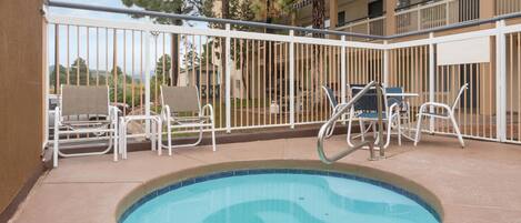 Una piscina con borde de azulejos, rodeada de barandillas de metal blanco y sillas de lounge blancas.