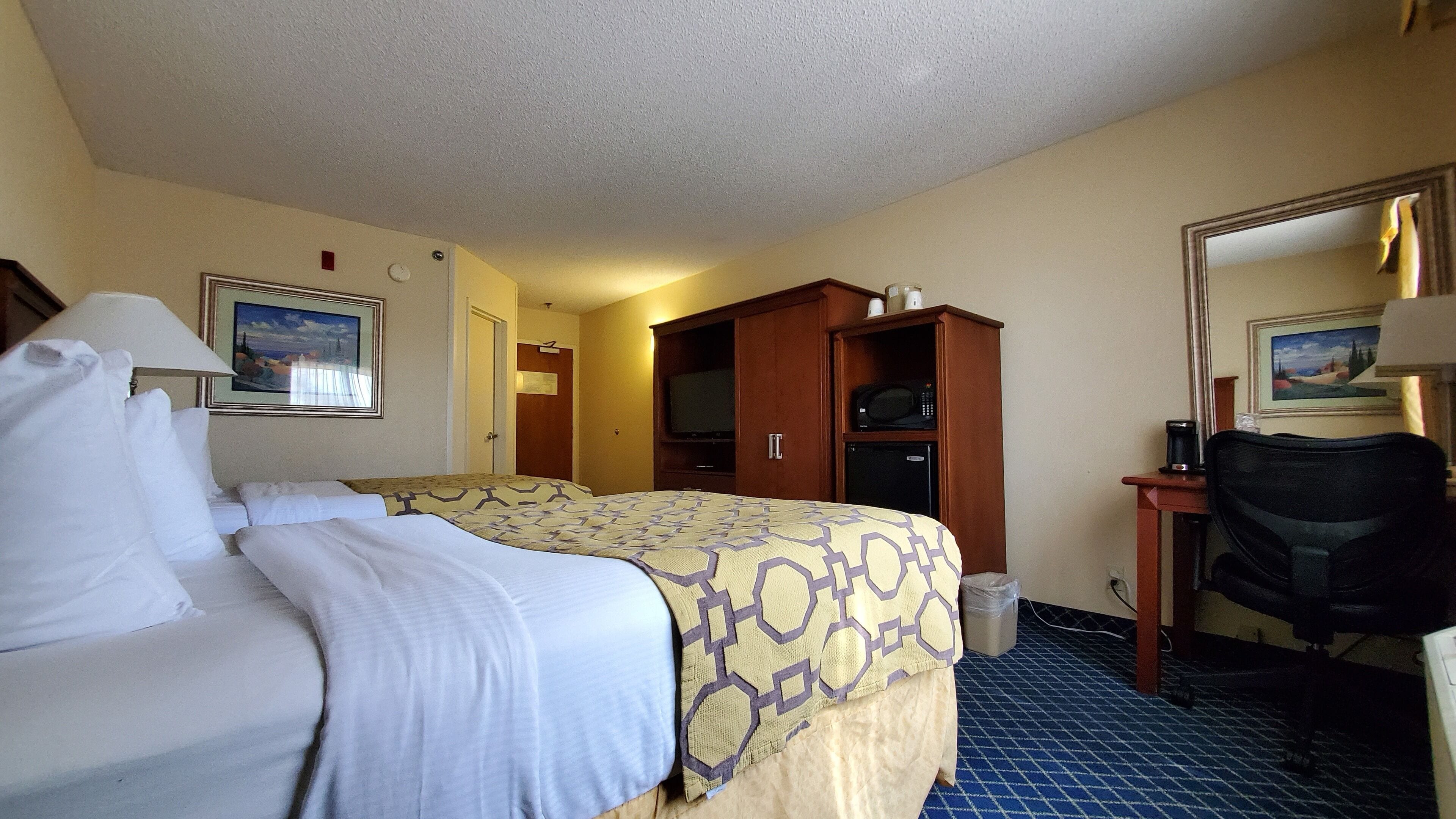 Quarto de hotel com cama, escrivaninha, cadeira, televisão e micro-ondas.