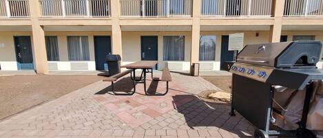 Un espace extérieur aménagé avec un barbecue et des tables de pique-nique, situé devant un immeuble doté de balcons.