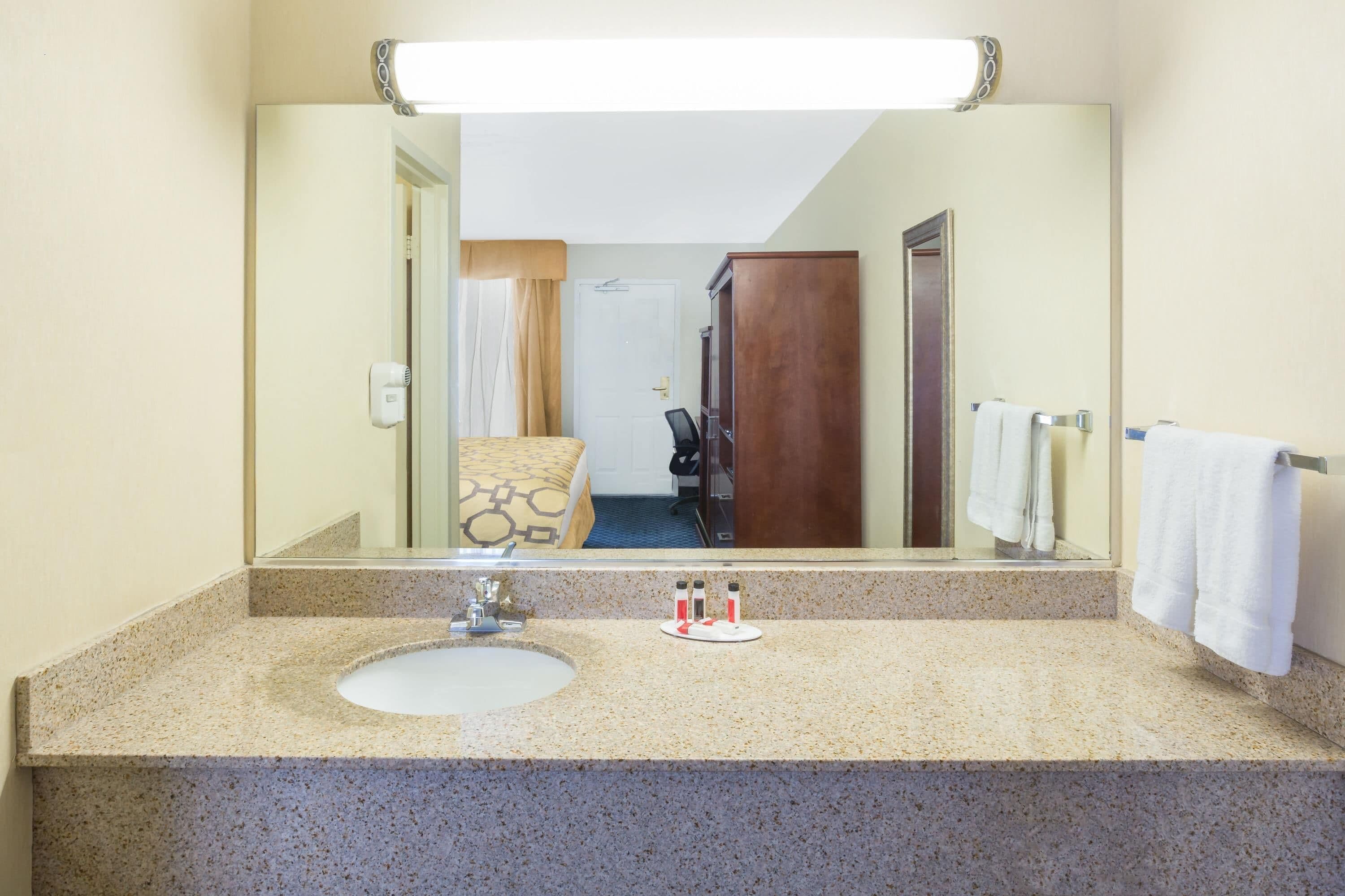A bathroom with a granite countertop, a sink, a mirror, and a towel rack.