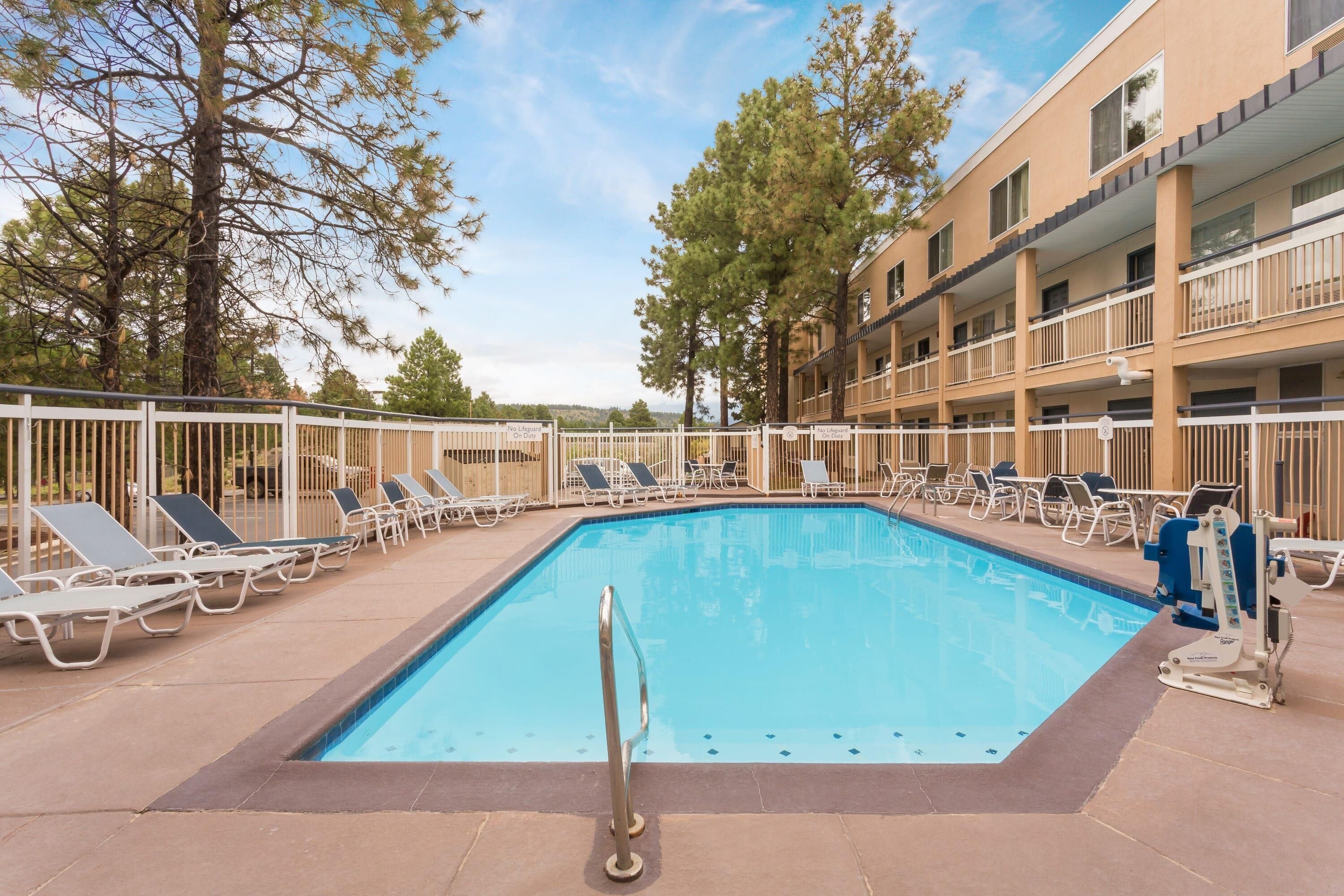 A rectangular pool with a metal ladder, surrounded by lounge chairs and a multi-story building with balconies.