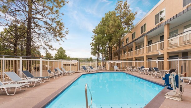 A rectangular pool with a metal ladder, surrounded by lounge chairs and a multi-story building with balconies. - Baymont by Wyndham Flagstaff (Flagstaff)